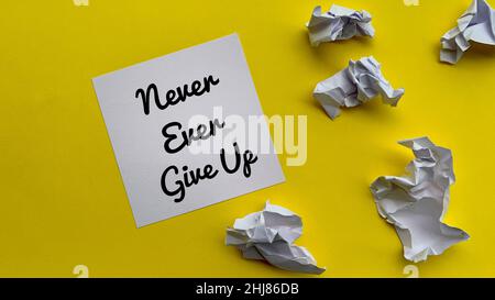 Top view of never ever give up text on notepad with trash papers and yellow background. Motivational concept. Stock Photo