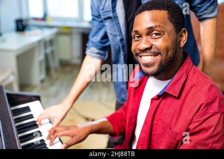 latin hispanic man learning to play on piano with caucasian teacher in classroom Stock Photo