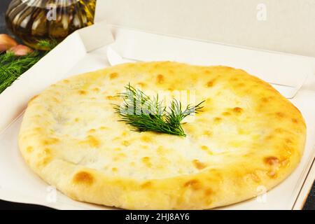Selective focus, Home baking delivery. A whole homemade freshly baked Ossetian pie with spinach, olive oil, parsley and garlic in a white open box. Fo Stock Photo