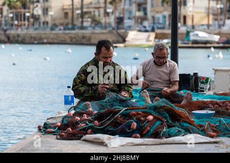 Marsaxlokk, Malta - 01 07 2022: Two fisherman knitting nets at the waterfront Stock Photo