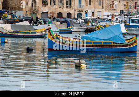 Marsaxlokk, Malta - 01 07 2022: Colorful boats at the harbor with the village in the harbor Stock Photo