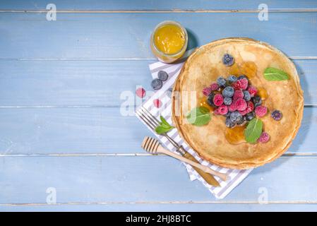 Russian Ukrainian European holiday Maslenitsa. Traditional thin crepes pancakes, with berrry, jam and honey toppings on wooden blue table, top view co Stock Photo