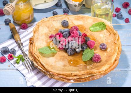 Russian Ukrainian European holiday Maslenitsa. Traditional thin crepes pancakes, with berrry, jam and honey toppings on wooden blue table, top view co Stock Photo