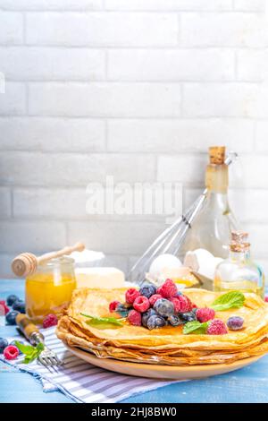 Russian Ukrainian European holiday Maslenitsa. Traditional thin crepes pancakes, with berrry, jam and honey toppings on wooden blue table, top view co Stock Photo