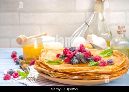 Russian Ukrainian European holiday Maslenitsa. Traditional thin crepes pancakes, with berrry, jam and honey toppings on wooden blue table, top view co Stock Photo