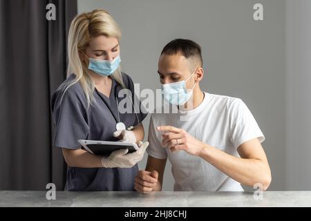 Female professional doctor showing medical test result explaining prescription using digital tablet app visiting man patient. Stock Photo