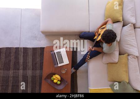 Directly above shot of african american young man playing guitar while with laptop at home. unaltered, music, wireless technology, lifestyle, food, dr Stock Photo