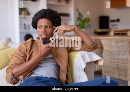 African american young man looking away while talking on call at home. unaltered, lifestyle, leisure activity, wireless technology, communication and Stock Photo