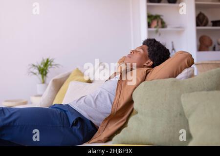 African american young man with eyes closed and hands behind head relaxing on sofa at home. unaltered, sleeping, relaxation, resting, lifestyle, leisu Stock Photo