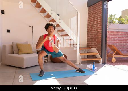 Full length of african american young man doing side squats on exercise mat at home. unaltered, fitness, stretching, drink, balance and active lifesty Stock Photo