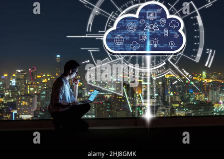 Asian businessman sitting and using the laptop and working with virtual screen connecting with cloud technology over the cityscape background at night Stock Photo