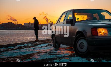 Person standing between car end waterfront durring sunset Stock Photo