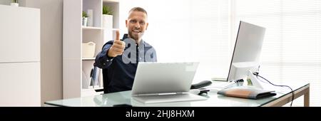 Happy Young Businessman Using Laptop At Desk In Office Stock Photo
