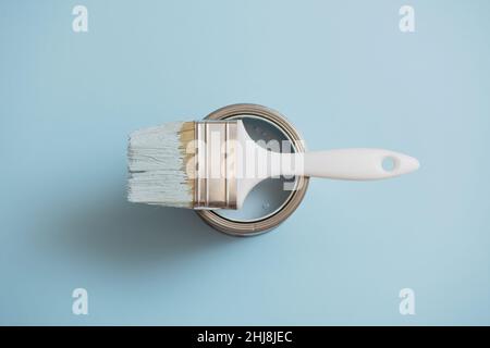 Top view of paint brush lying on open can of blue paint on blue background. Stock Photo