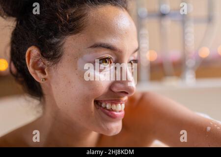 Closeup of smiling beautiful biracial young woman looking away in bathtub at spa. unaltered, spa, body care, lifestyle, vitiligo and wellness. Stock Photo