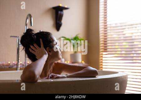 Thoughtful biracial young woman leaning on bathtub at spa. unaltered, spa, body care, lifestyle, loneliness, vitiligo and wellness. Stock Photo