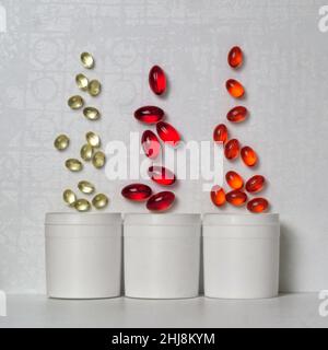 Multi-colored capsules with medicines or vitamins fly out of three white plastic jars Stock Photo