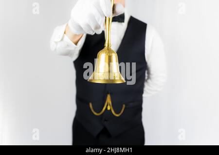 Portrait of Butler or Waiter in Black Waistcoat and White Gloves Holding Gold Bell. Stock Photo