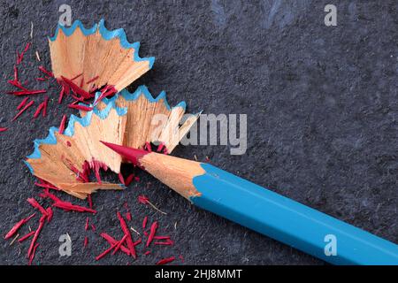 Single coloured pencil sharpened to a fine point with the wooden shavings on a dark background Stock Photo