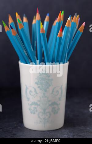 A pretty ceramic pot full  of Derwent artist's coloured pencils in a variety of colours on a dark background Stock Photo