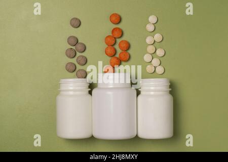 Multi-colored pills with medicines or vitamins fly out of three white plastic jars on a green background Stock Photo