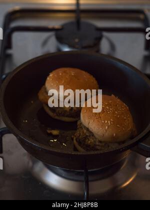 Vertical view of mini veggie hamburgers being heated up in a frying pan. Stock Photo