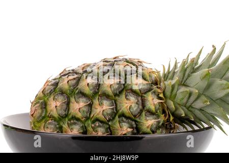 One sweet organic pineapple with a black ceramic plate, close-up, isolated on white. Stock Photo
