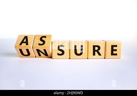 Assure or unsure symbol. Turned wooden cubes and changed the concept word unsure to assure. Beautiful white table, white background, copy space. Busin Stock Photo