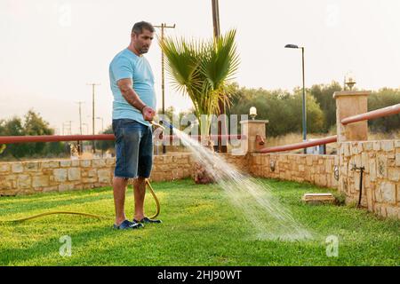 Man watering the lawn with a hose in the morning Stock Photo