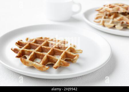 Waffles on white plates close-up and a cup of milk on a white table, tasty breakfast concept Stock Photo