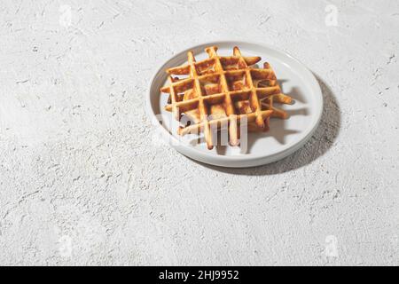 Freshly baked Belgian waffles on a white plate on a light table, copy space Stock Photo