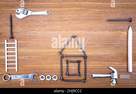 House shape made from screws and nails with hand tools and nuts arranged on a wooden background. House overhaul project concept. Stock Photo
