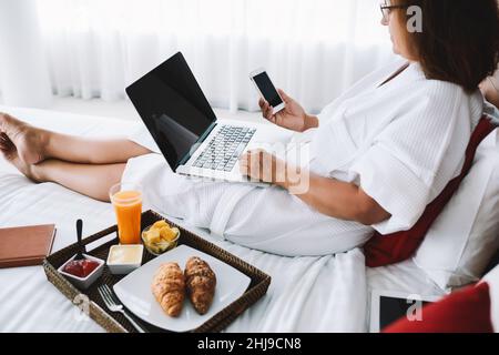 Crop woman using gadgets on hotel bed with breakfast Stock Photo