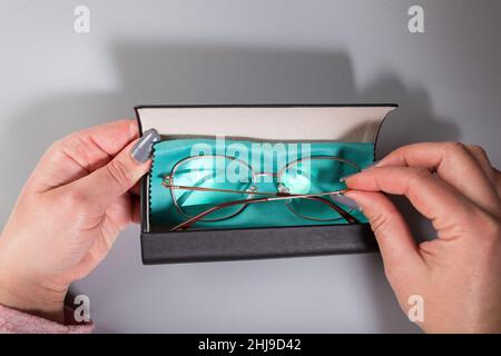 Female hands holding eye glasses in case with cleaning cloth. on grey background. Stock Photo