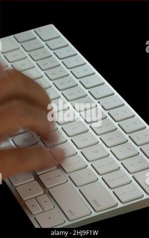 Blurred fingers working fast on white and silver keyboard. Closeup with black background and text space. Stock Photo