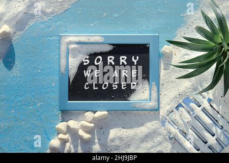 Sorry we are closed sign on blackboard. Sand background with pebbles, stones and seashells. Stock Photo