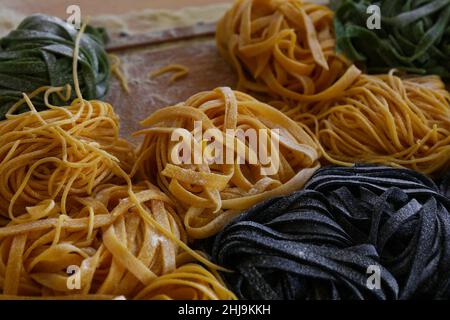 Close up cooking fresh handmade traditional Italian tagliatelle pasta, uncooked black, green and classical past on wooden table, high angle view Stock Photo
