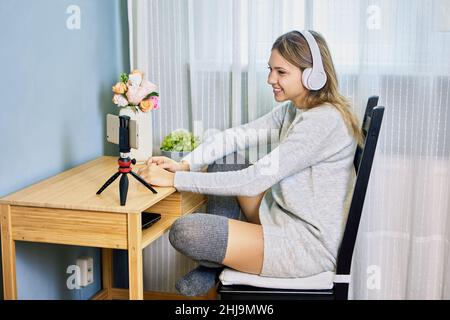 Live streaming by woman in headphones who uses handy on tripod. Stock Photo