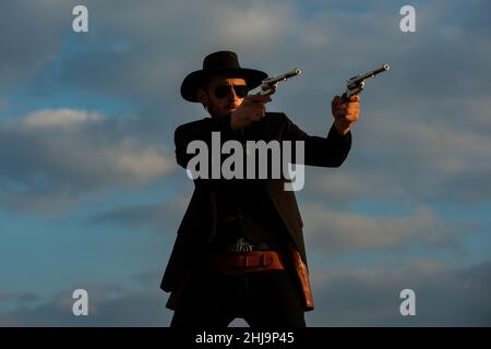 Cowboy shooting. Sheriff officer in black suit and cowboy hat. Man with wild west guns, vintage pistol revolver and marshal ammunition. US Marshals Stock Photo