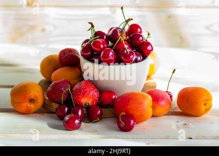 Fresh, juicy fruits, strawberries and nectarines on the table, cherries in a traditional wooden bowl, photographed in warm light Stock Photo