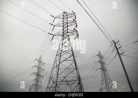 Tall metal electrical transmission power lines against a grey cloud background. Stock Photo
