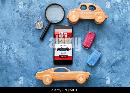 Mobile phone with open car rent app, toys, keys, magnifier and compass on grunge background Stock Photo