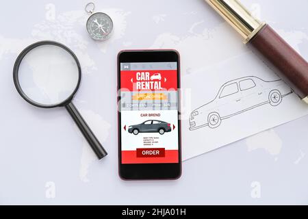 Mobile phone with open car rent app, magnifier, compass, drawn auto and spyglass on world map Stock Photo