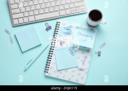 Stationery, cup of coffee, computer keyboard, sticky notes with text SHOPPING LIST and DON'T FORGET on blue background Stock Photo