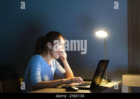Asian woman businessman working on her laptop to prepare for the presentation tomorrow morning at night she looked so sleepy and tired that she yawned Stock Photo