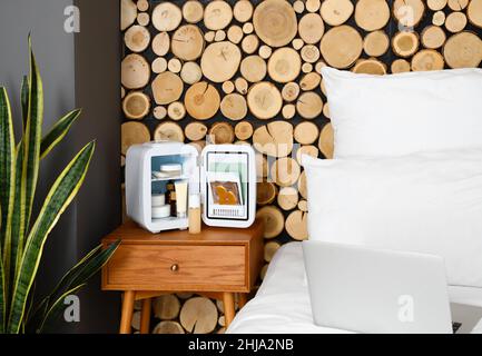 Small cosmetic refrigerator on bedside table near wooden wall Stock Photo