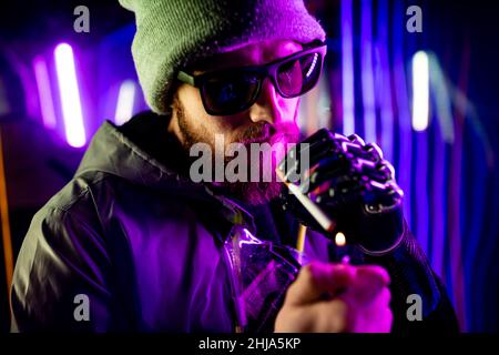 cyber robot hand close up of male handle use lighters going to smoking a cigarette in neon studio Stock Photo