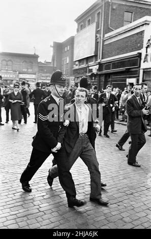 A large crowd gathered in Ridley Road, E8 to demonstrate against former fascist leader Sir Oswald Mosley and members of his anti-Semitic Blackshirt group who had planned a rally in London's East End. Mosley and his group were assaulted and punched to the ground as soon as his meeting opened at Ridley Road, Dalston. Police closed the meeting within the first three minutes and made 54 arrests, one of which was Sir Oswald's son Max.  Police arrest one of the angry demonstrators. 31st July 1962. Stock Photo