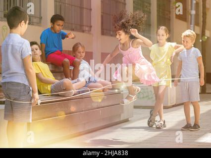 Energetic kids playing and skipping on elastic jumping rope in yard Stock Photo