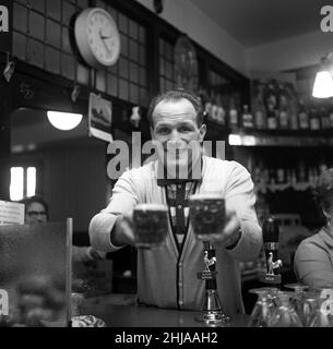 Henry Cooper at Bellingham in training for his 24th February date at Belle Vue Manchester where he defends his titles against Blackpool's Brian London. He trains underneath a pub, The Ship Inn, Bellingham. Pictured, Henry behind the bar of his training HQ pub, pulling half pints of bitter for customers. 4th February 1964. Stock Photo